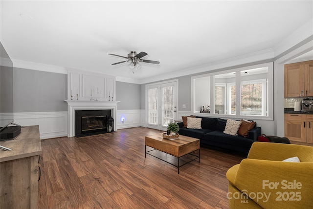 living room with a large fireplace, dark wood-type flooring, ceiling fan, and crown molding