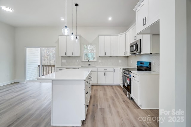 kitchen with stainless steel appliances, a kitchen island, a sink, light countertops, and decorative backsplash