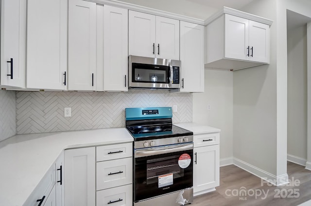 kitchen with light wood finished floors, tasteful backsplash, white cabinets, stainless steel appliances, and light countertops