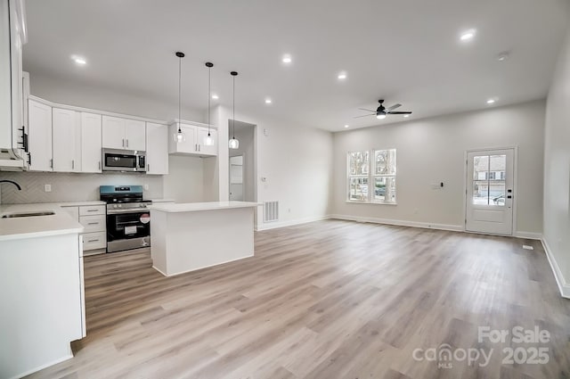 kitchen featuring a center island, light wood finished floors, stainless steel appliances, light countertops, and decorative backsplash