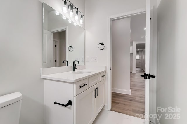 half bath with toilet, marble finish floor, vanity, and baseboards