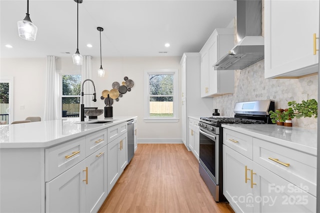 kitchen with appliances with stainless steel finishes, pendant lighting, white cabinetry, sink, and wall chimney exhaust hood