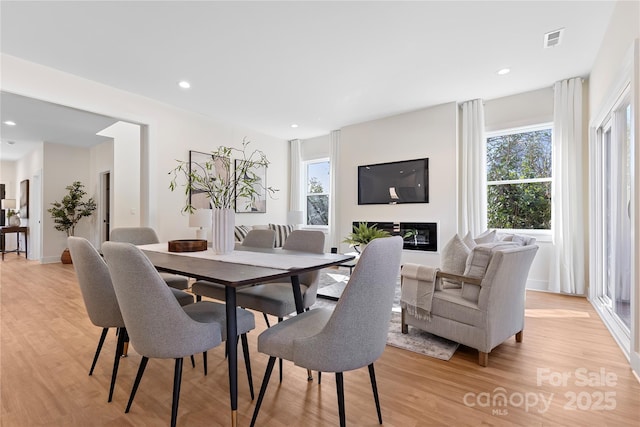 dining area with visible vents, recessed lighting, light wood-style floors, and a glass covered fireplace