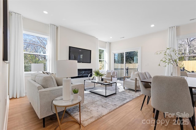 living area with a glass covered fireplace, recessed lighting, visible vents, and light wood finished floors