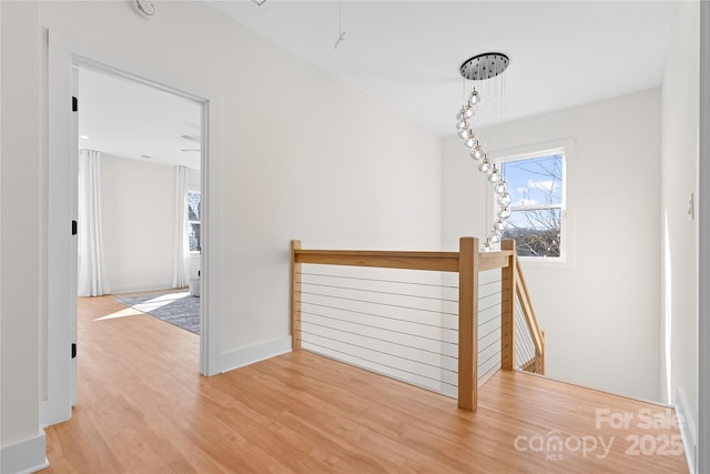 corridor with an upstairs landing, baseboards, and wood finished floors