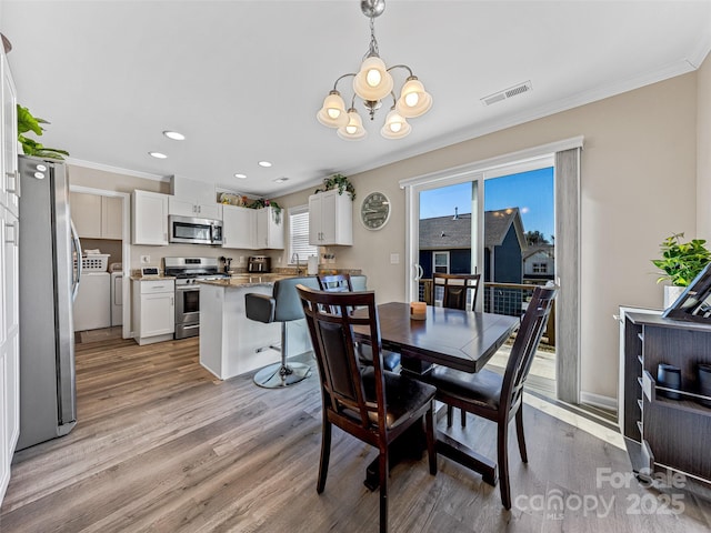 dining area featuring independent washer and dryer, light hardwood / wood-style flooring, crown molding, and a notable chandelier