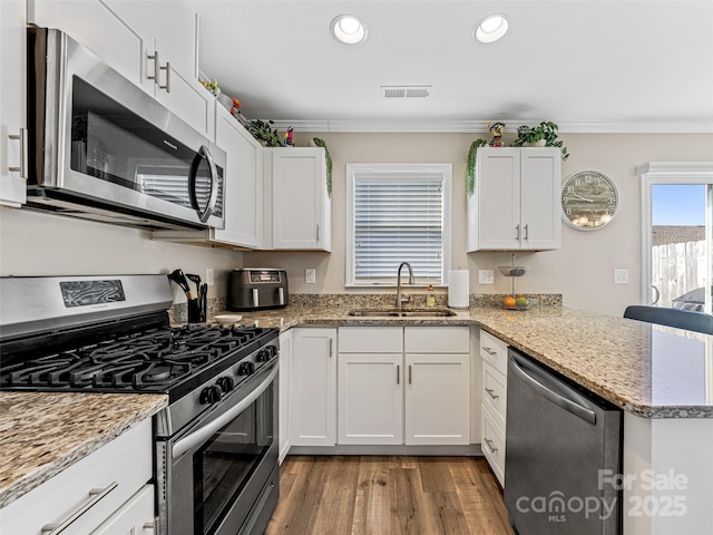 kitchen featuring kitchen peninsula, light stone countertops, stainless steel appliances, sink, and white cabinets