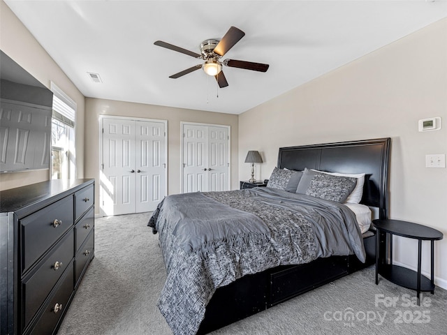 bedroom featuring two closets, light colored carpet, and ceiling fan