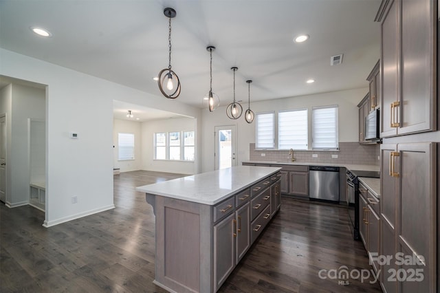 kitchen featuring pendant lighting, appliances with stainless steel finishes, tasteful backsplash, a kitchen island, and light stone counters