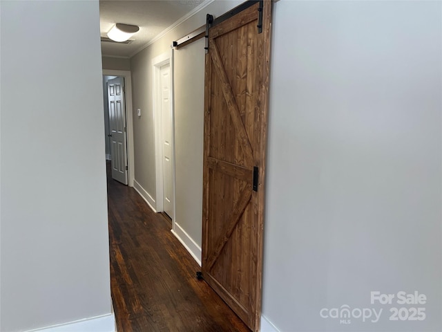 hall with a textured ceiling, dark wood-type flooring, ornamental molding, and a barn door