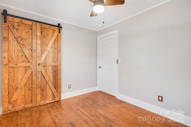 unfurnished bedroom featuring ceiling fan, a barn door, wood-type flooring, and crown molding