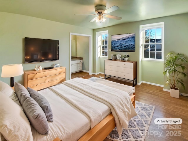 bedroom featuring multiple windows, ceiling fan, ensuite bath, and hardwood / wood-style flooring