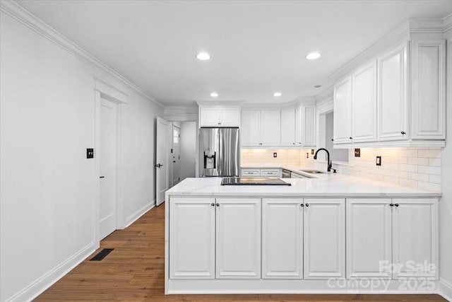 kitchen featuring sink, stainless steel refrigerator with ice dispenser, white cabinetry, kitchen peninsula, and tasteful backsplash