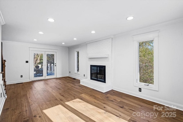 unfurnished living room featuring ornamental molding, plenty of natural light, a brick fireplace, and hardwood / wood-style floors