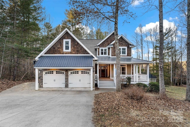 view of front of home with covered porch, an attached garage, metal roof, stone siding, and driveway