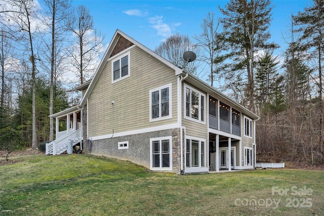 back of property featuring stone siding, a sunroom, and a lawn