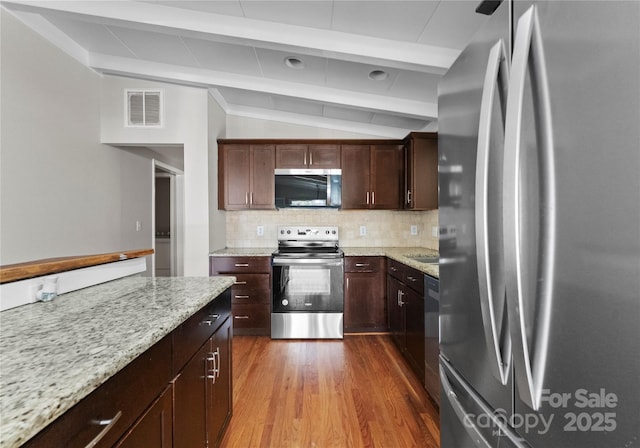 kitchen featuring appliances with stainless steel finishes, lofted ceiling with beams, light stone countertops, and decorative backsplash