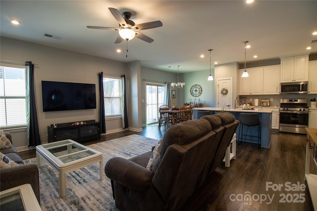 living room with ceiling fan with notable chandelier and dark wood-type flooring