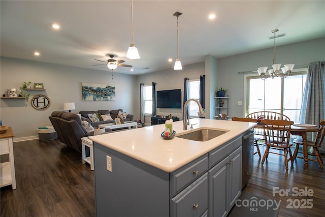 kitchen with sink, dark wood-type flooring, an island with sink, gray cabinets, and ceiling fan with notable chandelier