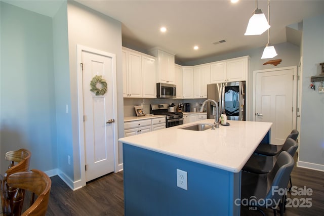 kitchen featuring sink, hanging light fixtures, stainless steel appliances, a center island with sink, and white cabinets