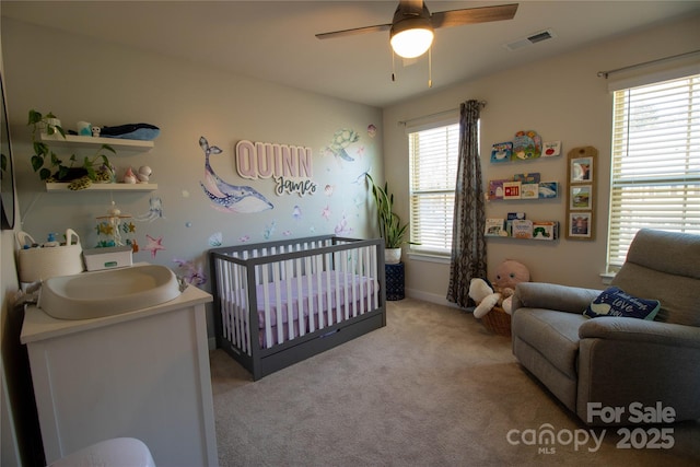 bedroom with ceiling fan, a crib, light carpet, and multiple windows