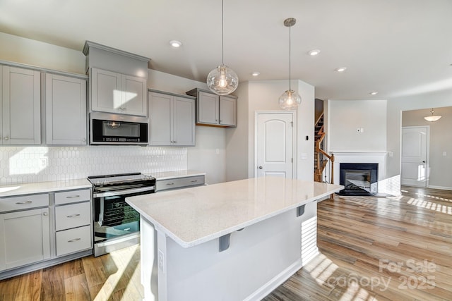 kitchen featuring gray cabinetry, backsplash, a kitchen breakfast bar, light stone counters, and stainless steel appliances