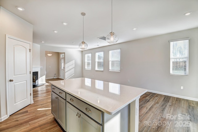 kitchen with pendant lighting, a center island, gray cabinets, light wood-type flooring, and light stone counters