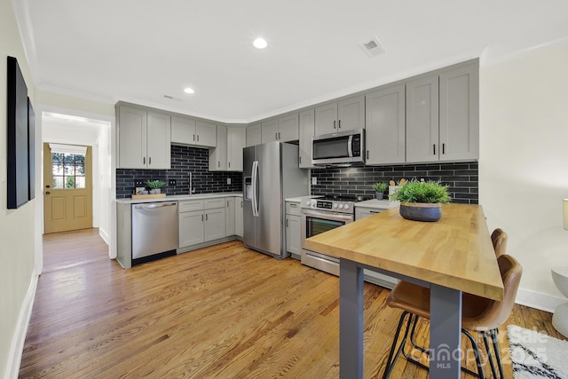 kitchen with sink, appliances with stainless steel finishes, gray cabinetry, ornamental molding, and light hardwood / wood-style floors