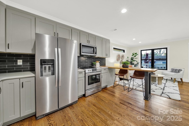 kitchen featuring gray cabinetry, decorative backsplash, light hardwood / wood-style flooring, and stainless steel appliances