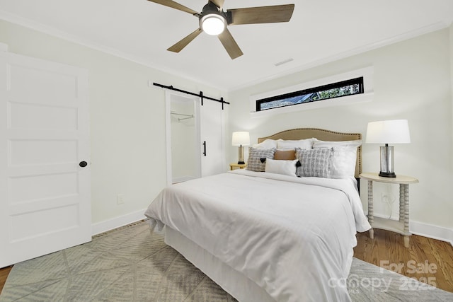 bedroom with light wood-type flooring, ornamental molding, a closet, ceiling fan, and a barn door