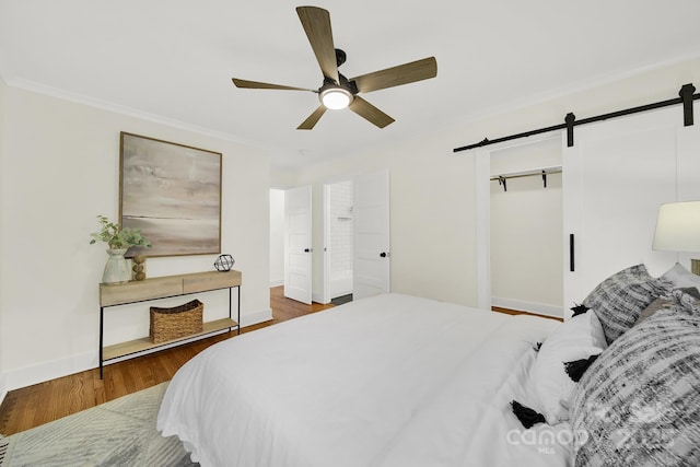 bedroom with hardwood / wood-style floors, ornamental molding, a barn door, and ceiling fan