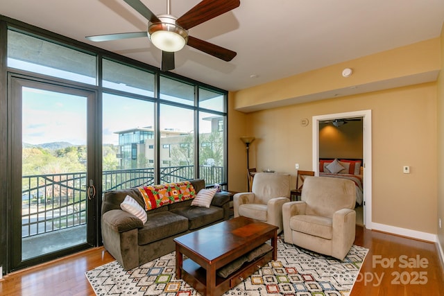 living room with a mountain view, light hardwood / wood-style flooring, a wall of windows, and ceiling fan