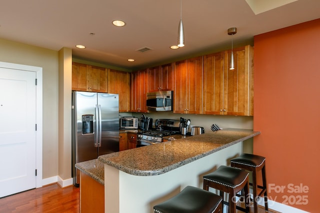 kitchen featuring a kitchen breakfast bar, kitchen peninsula, hanging light fixtures, and stainless steel appliances