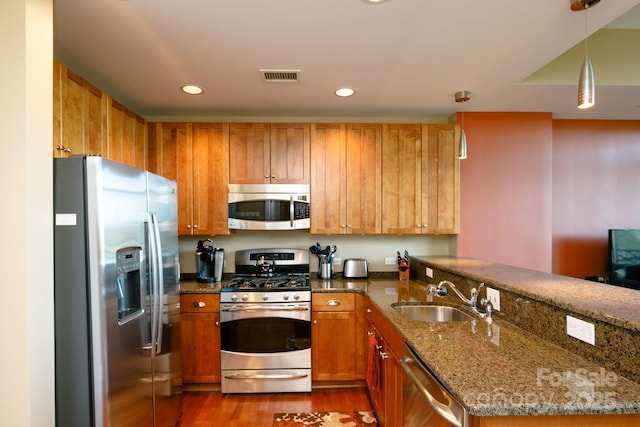 kitchen with sink, stainless steel appliances, kitchen peninsula, dark stone countertops, and decorative light fixtures