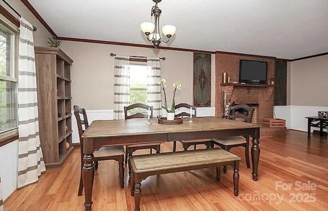 dining area featuring light hardwood / wood-style floors, a brick fireplace, a notable chandelier, and crown molding