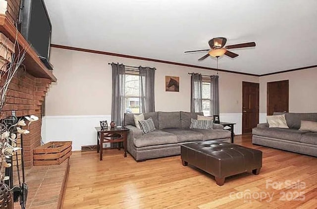 living room featuring crown molding, ceiling fan, light wood-type flooring, and a brick fireplace