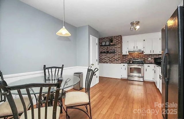 kitchen featuring stainless steel electric stove, black fridge, white cabinets, and hanging light fixtures