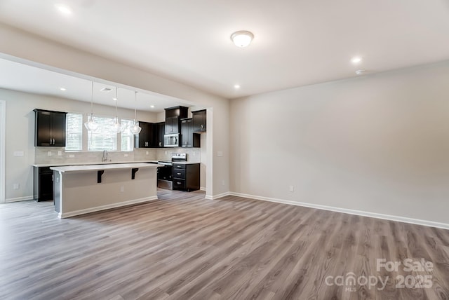 kitchen with pendant lighting, a center island, backsplash, light wood-type flooring, and appliances with stainless steel finishes