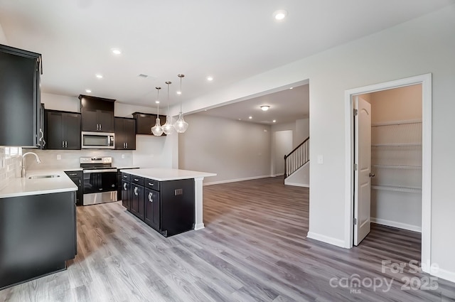 kitchen with a center island, sink, stainless steel appliances, pendant lighting, and light hardwood / wood-style floors