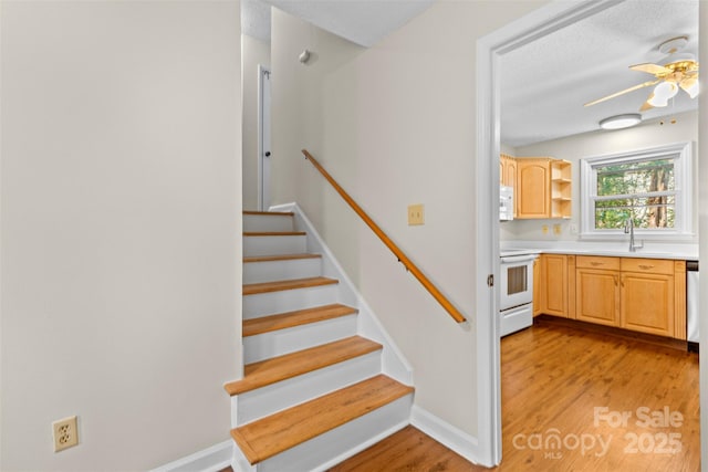 stairway with sink, hardwood / wood-style flooring, a textured ceiling, and ceiling fan