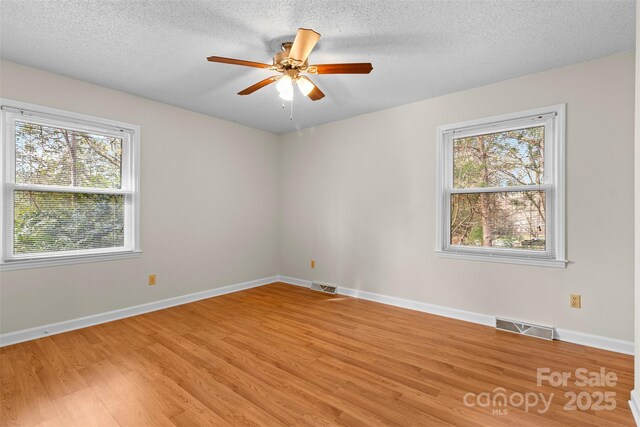 unfurnished room featuring ceiling fan, hardwood / wood-style floors, a textured ceiling, and plenty of natural light