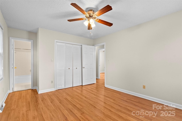 unfurnished bedroom featuring light hardwood / wood-style flooring, a closet, a textured ceiling, ensuite bathroom, and ceiling fan