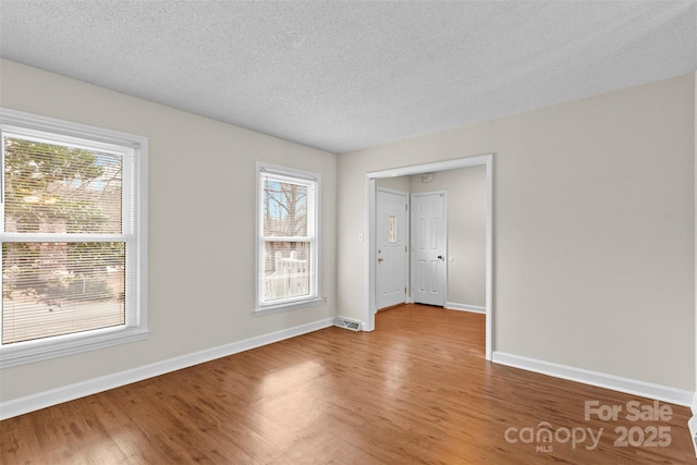 unfurnished room with a textured ceiling, hardwood / wood-style floors, and a healthy amount of sunlight