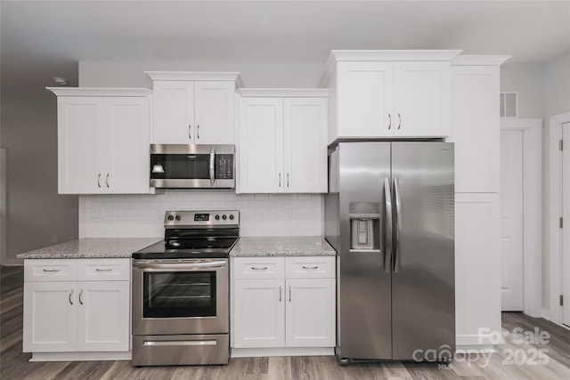 kitchen with white cabinets, stainless steel appliances, decorative backsplash, and light stone countertops