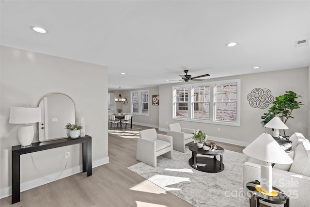 living room with ceiling fan with notable chandelier and light wood-type flooring