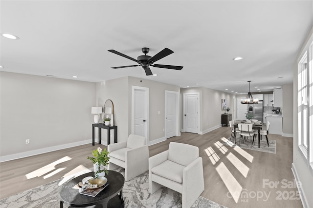 living room with a wealth of natural light, ceiling fan with notable chandelier, and light wood-type flooring