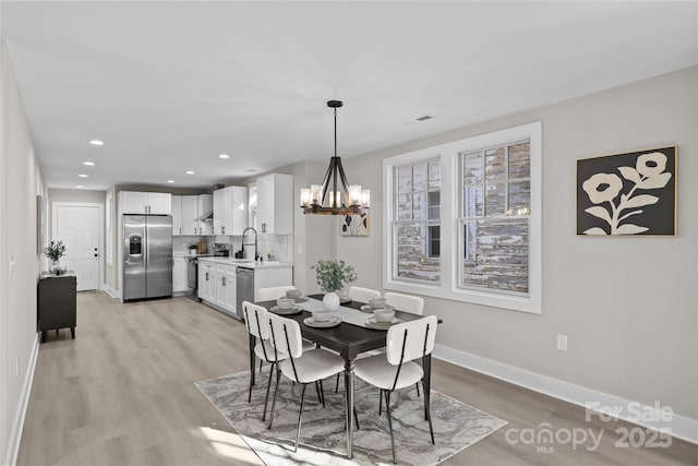 dining area featuring an inviting chandelier, sink, and light wood-type flooring