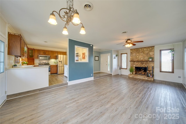 unfurnished living room featuring a stone fireplace, plenty of natural light, light hardwood / wood-style floors, and ceiling fan with notable chandelier