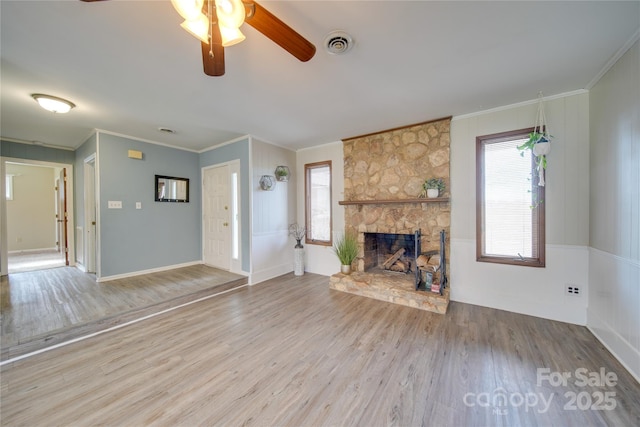 unfurnished living room featuring hardwood / wood-style flooring, a stone fireplace, ceiling fan, and ornamental molding