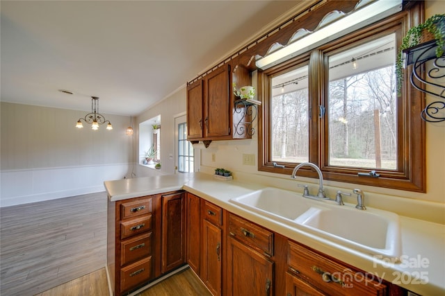 kitchen with kitchen peninsula, dark hardwood / wood-style flooring, sink, a notable chandelier, and hanging light fixtures